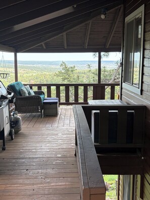 A wooden deck with a view of a landscape, a wicker chair, a table, and a grill.