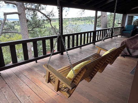 A wooden swing chair on a porch with a view of a green landscape.. Built in 1908 this historic cabin is full of original charm with a penthouse view. Step inside and you are immediately greeted by a full unobstructed view of Elephant Rock. Sleeping up to 9 people.