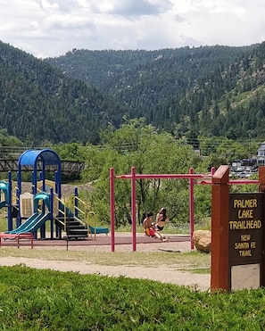 En legeplads med gynger og rutsjebaner, et skilt for Palmer Lake Trailhead, og et bjerg i baggrunden.