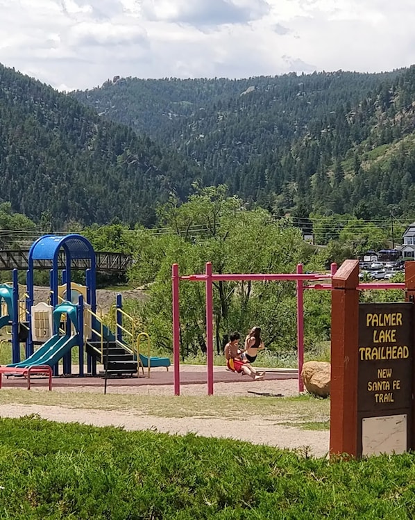 Ein Spielplatz mit Schaukeln und Rutschen, ein Schild für Palmer Lake Trailhead und ein Berg im Hintergrund.