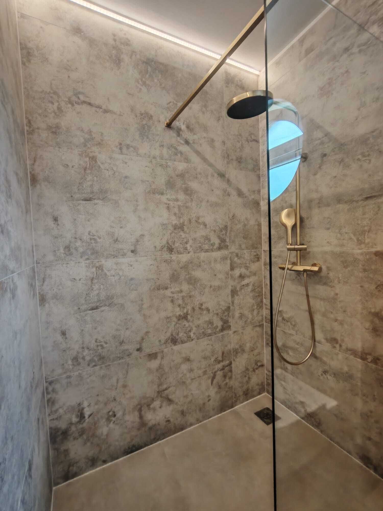 Une douche avec une porte en verre, un pommeau de douche à main et un flexible de douche à main.