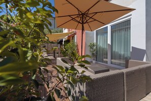 Eine Terrasse mit Korbmöbeln, einem großen Sonnenschirm und einer Steinmauer.