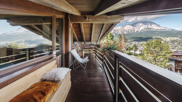Een balkon met houten balken, een comfortabele bank en uitzicht op een berg.