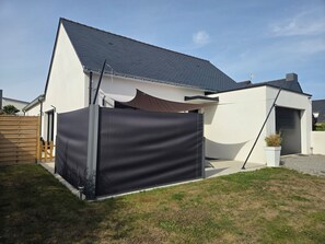 Ein modernes Haus mit Satteldach, schwarzem Sichtschutz und einem kleinen Gartenbereich.