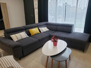 Ein modernes Wohnzimmer mit einem dunkelgrauen Ecksofa, einem weißen Couchtisch und einem kleinen Blumentopf.