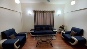 Uma sala de estar com um sofá, duas poltronas, uma mesa de centro, uma cortina e uma pequena mesa com um vaso.