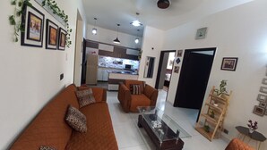 Sala de estar com sofá, poltrona e mesa de centro. Cozinha visível ao fundo, com micro-ondas e armários.