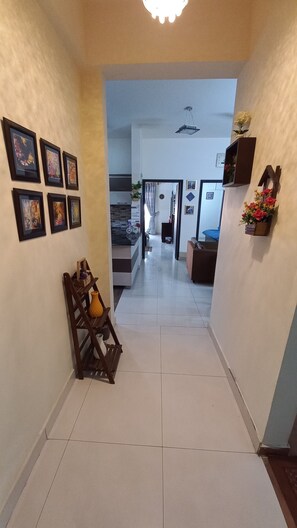 Un couloir dont les murs sont ornés de tableaux encadrés, un banc en bois avec un vase, et une plante en pot.