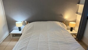 Una camera da letto con un letto, due comodini con lampade, una parete grigia e un pavimento piastrellato.