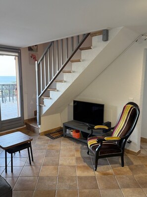 A living room with a TV, a striped armchair, a small table, and a staircase. - Beautiful Mazet in Pramousquier, Le Lavandou, with Terrace, 3 Bedrooms Sea View. (LE LAVANDOU)