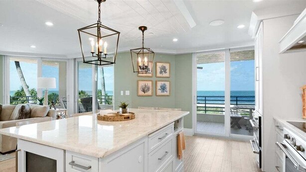A modern kitchen with a large island, white cabinetry, and a view of the ocean. - Beachfront 3BR/3BA condo with pool, WiFi, and heated outdoor pool. (Marco Island)