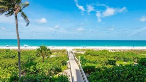 A pathway leading to a beach with palm trees and a clear blue sky. - Beachfront 3BR/3BA condo with pool, WiFi, and heated outdoor pool. (Marco Island)
