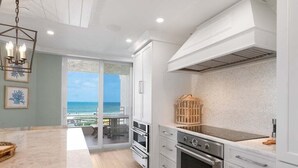 A modern kitchen with white cabinetry, stainless steel appliances, and a view to the outside. - Beachfront 3BR/3BA condo with pool, WiFi, and heated outdoor pool. (Marco Island)