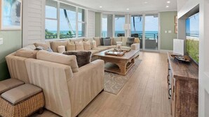 A spacious living room with a large sectional sofa, a coffee table, and a view of the ocean through large windows. - Beachfront 3BR/3BA condo with pool, WiFi, and heated outdoor pool. (Marco Island)