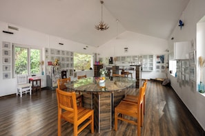 A spacious kitchen with a glass island, wooden chairs, and a large window with a view of greenery. - Lolos by Raho Cozy Loft Stay in Coorg (Virajpet)