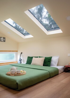 Ein Schlafzimmer mit Oberlicht, einem Bett mit grün-weißer Bettwäsche, einer Gitarre und einem Tablett mit Tassen und einem Teekessel.