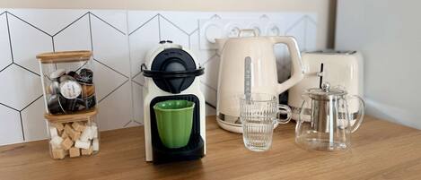 Una encimera de cocina con una cafetera, un tarro de cristal con cubitos de azúcar, una taza verde y una tetera.