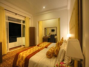Ein Hotelzimmer mit zwei Betten, einem Schreibtisch, einem Stuhl, einem Spiegel und einer Glastür zum Balkon.