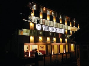 Ein Hotel namens 'The Queensbury' mit auffälliger Schrifttafel, mehreren Stockwerken und einer gut beleuchteten Fassade.