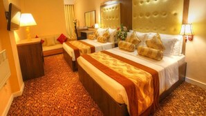 A hotel room with two beds, a sofa, a mirror, and a television. - Queensbury City Hotel - Nuwaraeliya (Nuwaraeliya)