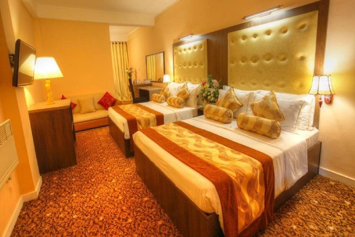 Ein Hotelzimmer mit zwei Betten, einem Sofa, einem Spiegel und einem Fernseher.