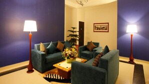 A room with two sofas, a coffee table with flowers, two floor lamps, and a painting on the wall. - Queensbury City Hotel - Nuwaraeliya (Nuwaraeliya)