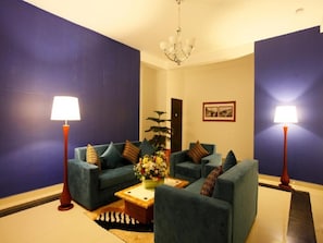 Ein Zimmer mit zwei Sofas, einem Couchtisch mit Blumen, zwei Stehlampen und einem Gemälde an der Wand.