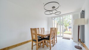 Un comedor con una mesa y sillas de madera, una lámpara de techo moderna y vistas a través de un ventanal.