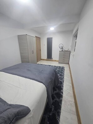 A bedroom with a bed, wardrobe, radiator, dresser, and a window.