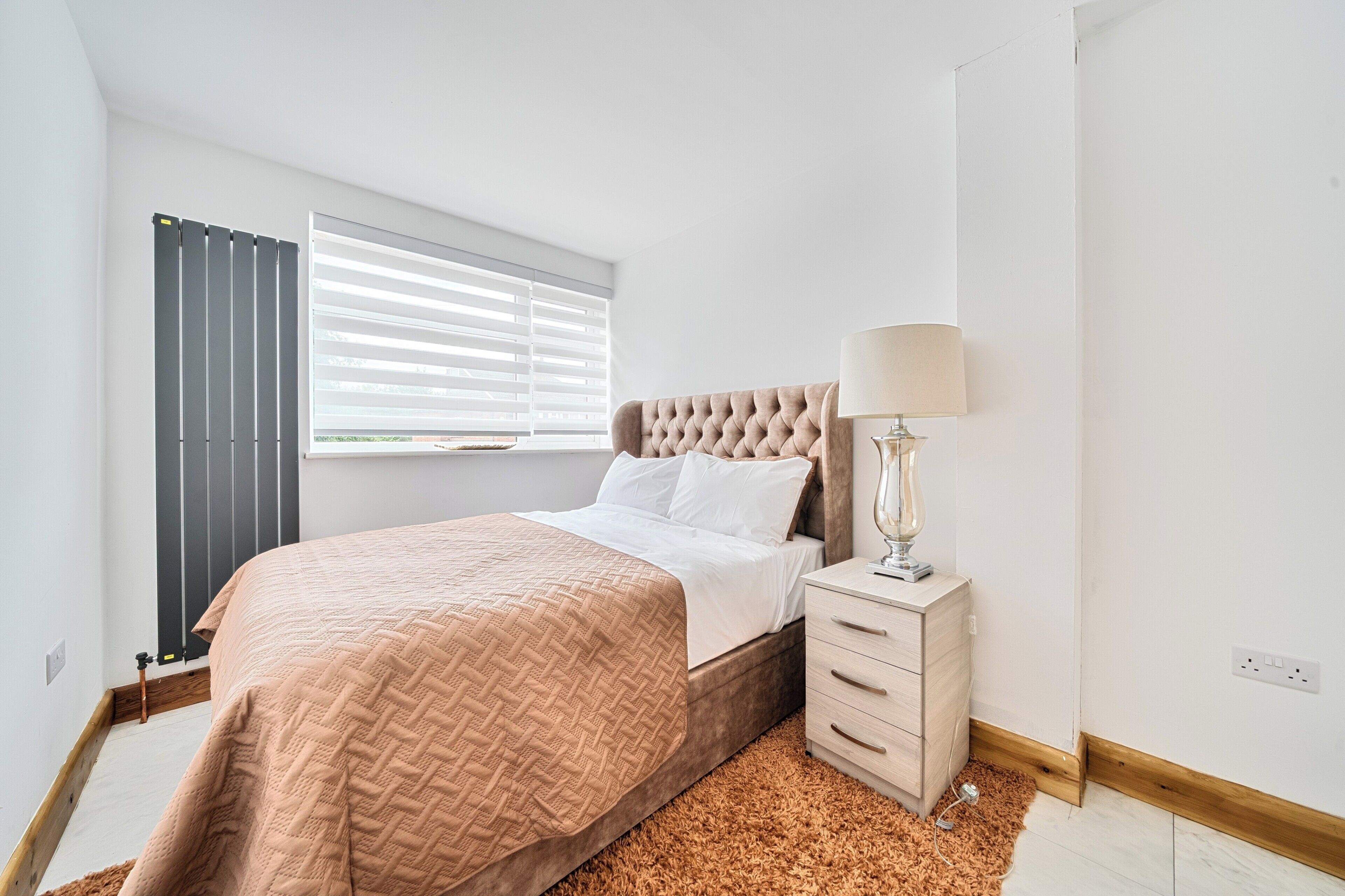 A bedroom with a bed, bedside table, lamp, and window with blinds.