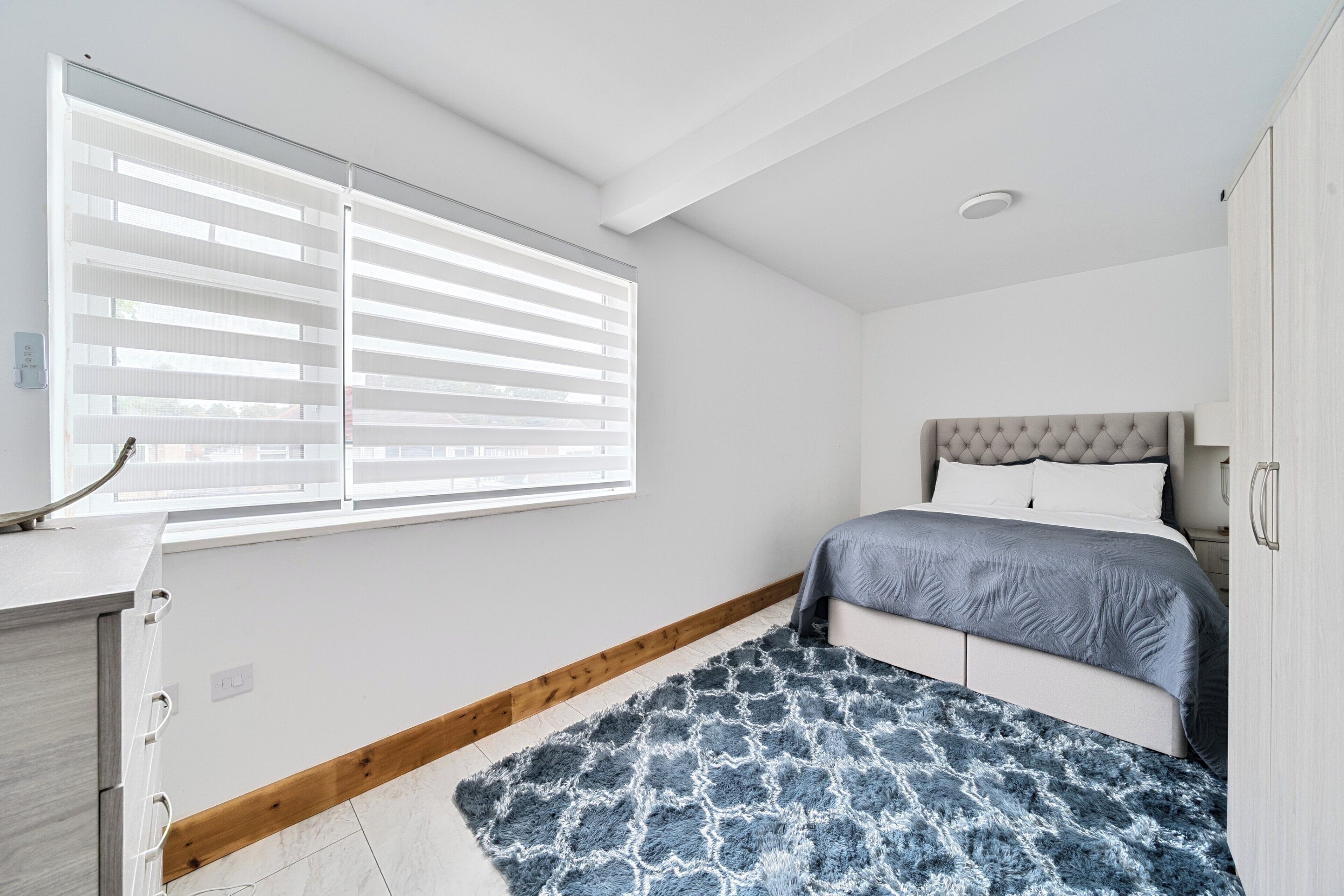 Un dormitorio con cama, ventana con persianas, escritorio y armario.