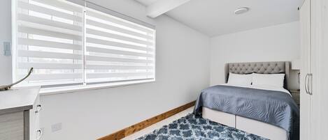 Un dormitorio con cama, ventana con persianas, escritorio y armario.