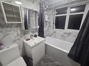 A bathroom with a white sink, a mirror, a toilet, a bathtub, and a window with a curtain.