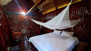 Een houten kamer met een bed, een plafondventilator en een klamboe.