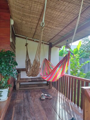 A wooden deck with a hammock, hanging macrame, and a pair of shoes.