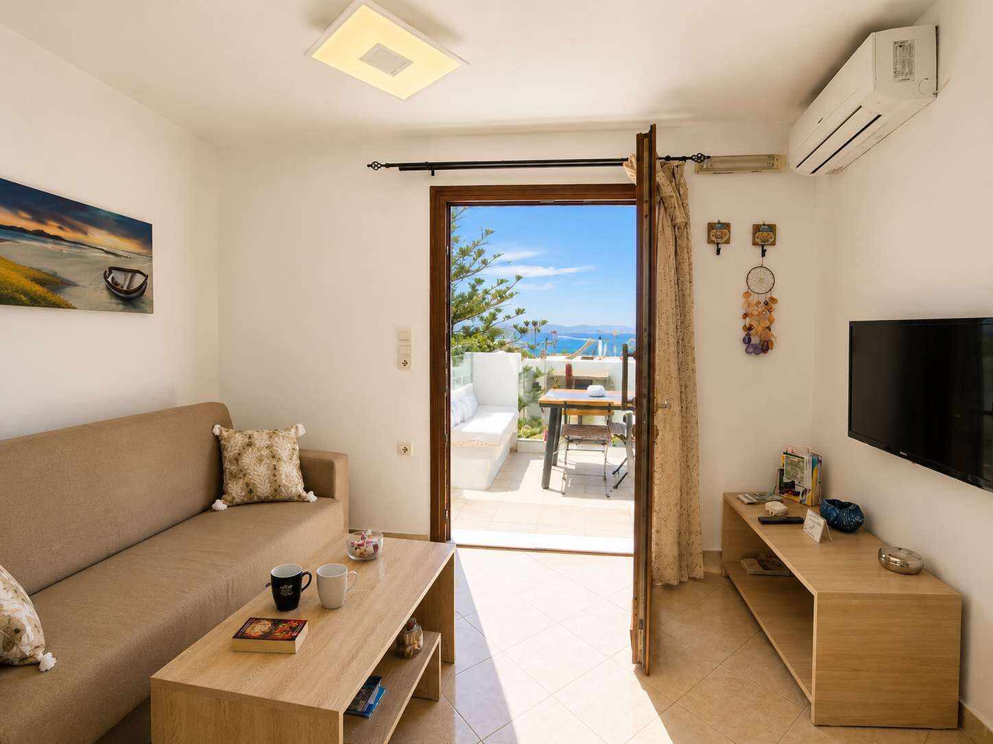 A modern living room with a sofa, coffee table, TV, and an open door leading to a balcony with a view.