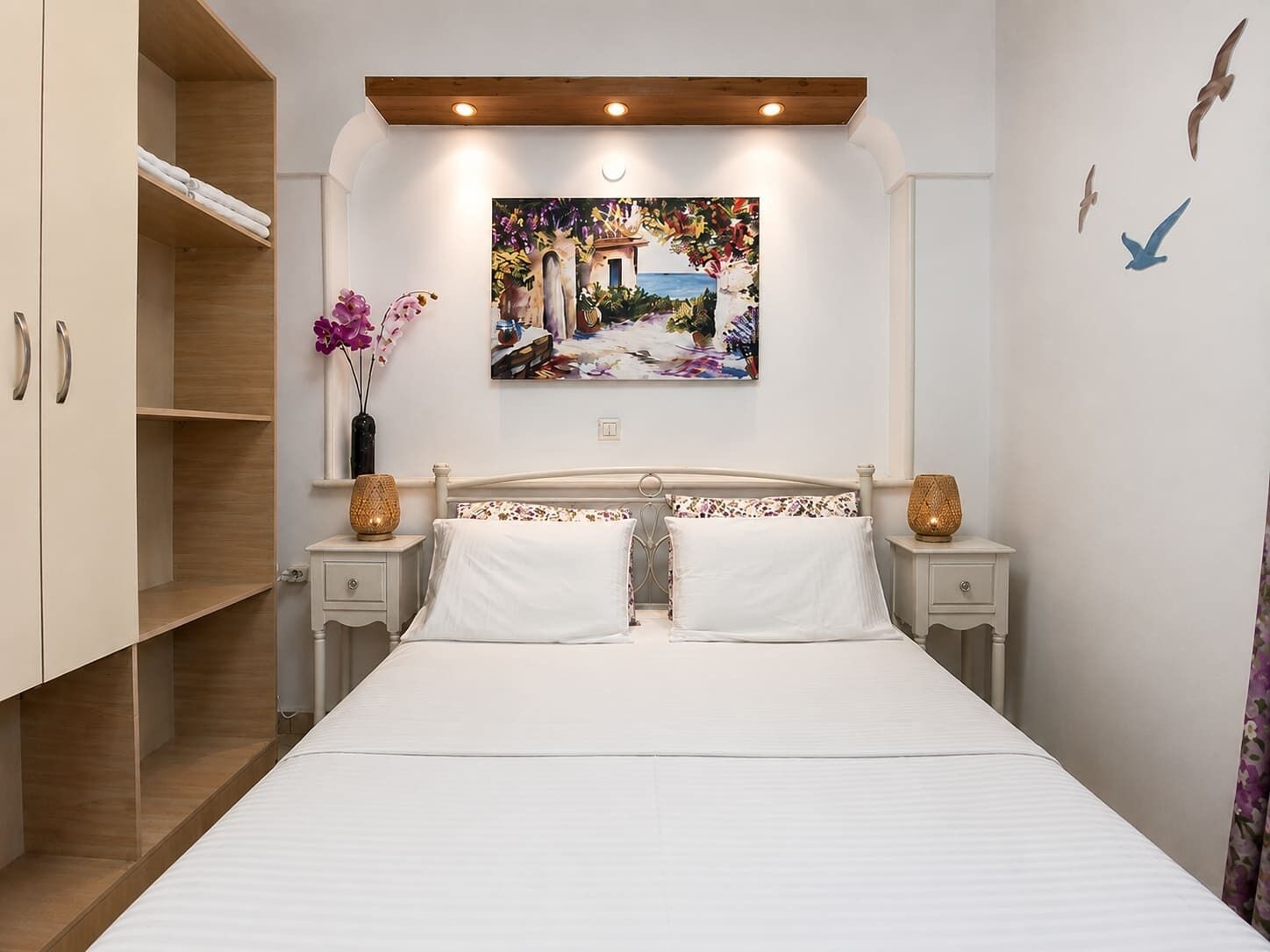 Een slaapkamer met een bed, twee nachtkastjes, een kledingkast en een schilderij aan de muur.
