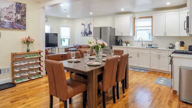 Una cocina moderna con armarios blancos, un refrigerador de acero inoxidable y un comedor con mesa de madera y sillas marrones.
