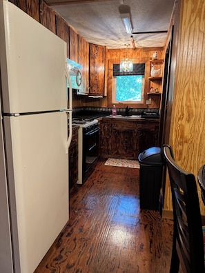 A compact kitchen with wooden cabinets, a white refrigerator, a stove, and a window.