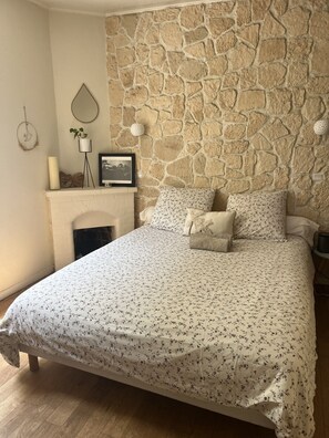 Ein Schlafzimmer mit Steinwand, Kamin, einem Bett mit Blumenmuster auf der Bettwäsche und einem Nachttisch.