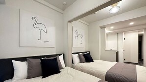 Ein Hotelzimmer mit zwei Betten, jeweils mit Kopfteil, weißer Bettwäsche und schwarzen sowie grauen Kissen. An den Wänden befinden sich zwei gerahmte Wandbilder mit Vogelmotiven.