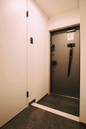 Un pasillo estrecho con una puerta al final, un pequeño escalón que lleva a la puerta y una lámpara fijada a la pared.