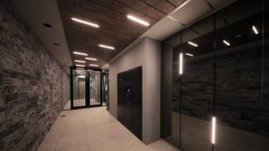 Ein Korridor mit einer Steinwand, einem Glaselevator und eingelassener Beleuchtung.