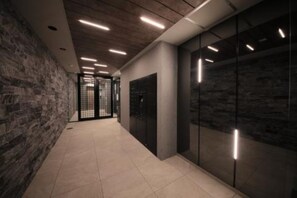 Un passadís amb paret de pedra, un ascensor de vidre i il·luminació empotrada.