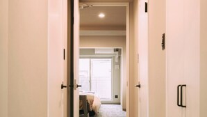 Ein Hotelkorridor mit Teppichboden, weißen Wänden und Türen zu einem Zimmer mit Bett und Fenster.