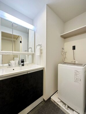 A bathroom with a white sink, dark cabinets, a mirror, and a white heater. - LIFEMENT GLANZ SAKAIMACHI (Hiroshimashi nakaku sakaimachi)
