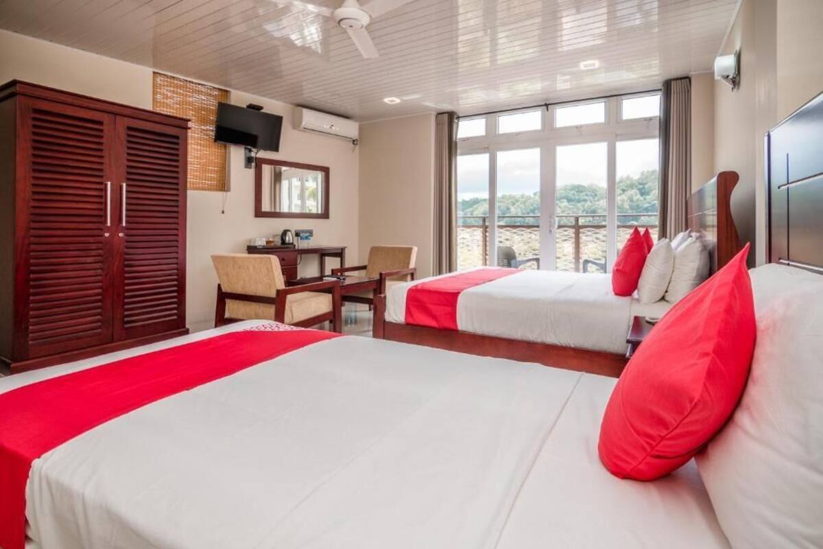 A hotel room with two beds, a desk, a chair, a wardrobe, and a large window with a view.