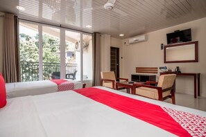 Een hotelkamer met twee bedden, een balkon, een bureau met stoelen en een televisie.