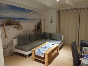 Ein Wohnzimmer mit einer Couch, einem Holztisch, einem Wandbild von einem Strand und einer Stehlampe.