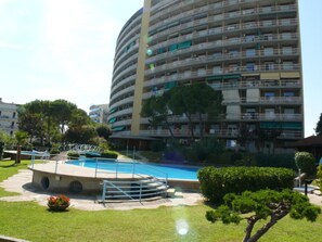 A multi-story hotel with a swimming pool, surrounded by greenery and other buildings. - Practical flat with pool just 100m from the beach (Lignano Sabbiadoro)
